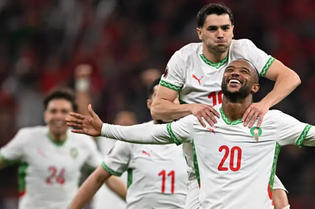 صورة للاعب منتخب مغربي وهو يقفز على أكتاف زملائه في الملعب أثناء احتفاله بتسجيل الهدف الثاني في مباراة المغرب وزامبيا التي انتهت بفوز المغرب 3-0.