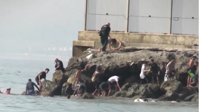 صورة تظهر حشدًا من المهاجرين يتسلقون تلة بعد السباحة الجماعية إلى سبتة، إسبانيا.